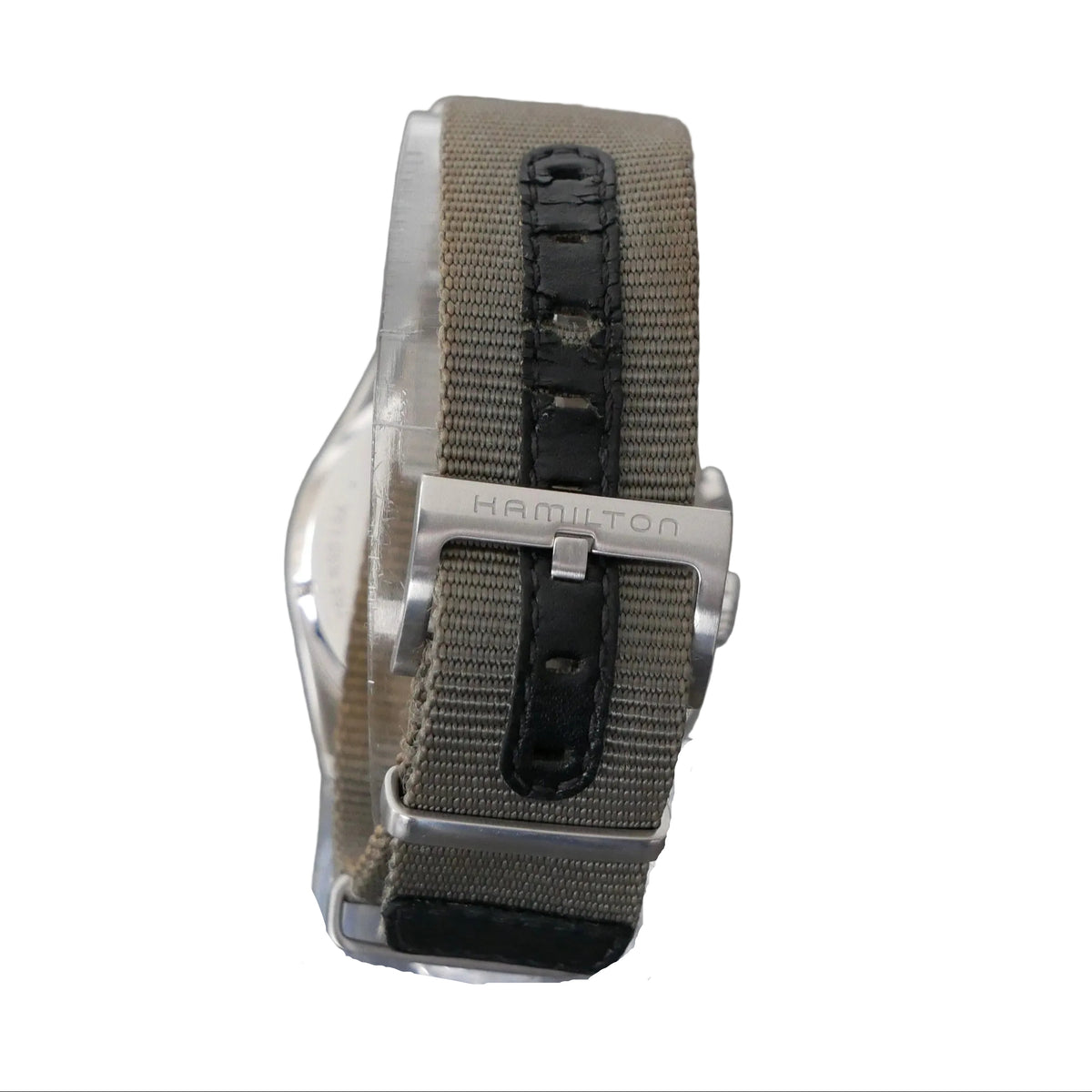 A close-up of a Hamilton watch band in olive drab canvas and black leather, mounted on a clear plastic display stand against a textured gray background.